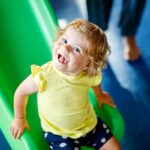 preschooler smiles up at camera while sliding down a green slide