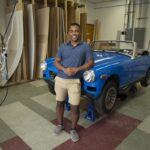 Tiree Walker stands in front of the MG Midget car he is working on for a 3D scanning research project.